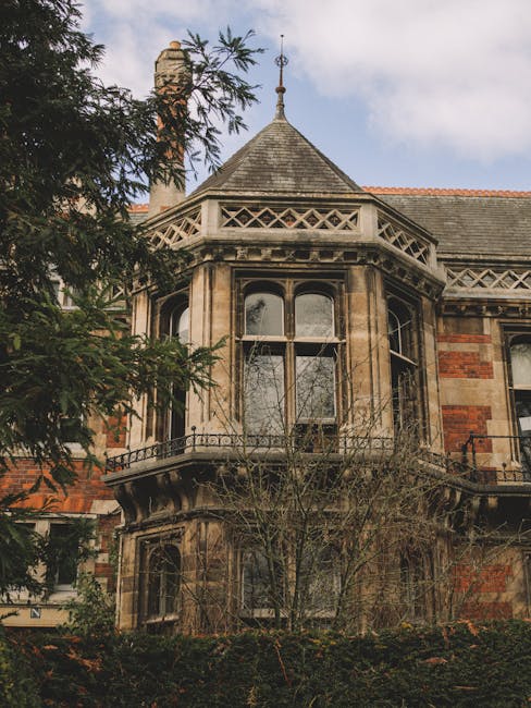 Exterior view of a historic Victorian-style house with a prominent rounded bay window on the upper floor adorned with decorative stonework and a small ornate balcony railing. The building features a steep, conical slate roof topped with a decorative finial, and its façade displays a mixture of red brick and stone detailing. Surrounding the house are trees and bushes, some with bare branches, indicating a possible winter or early spring season. This property illustrates a classic architectural style often encountered in house removals and property relocations, relevant to services provided by Man with Van Forest Hill for transporting or relocating homes within the Forest Hill area as part of their home relocation and furniture transport offerings.